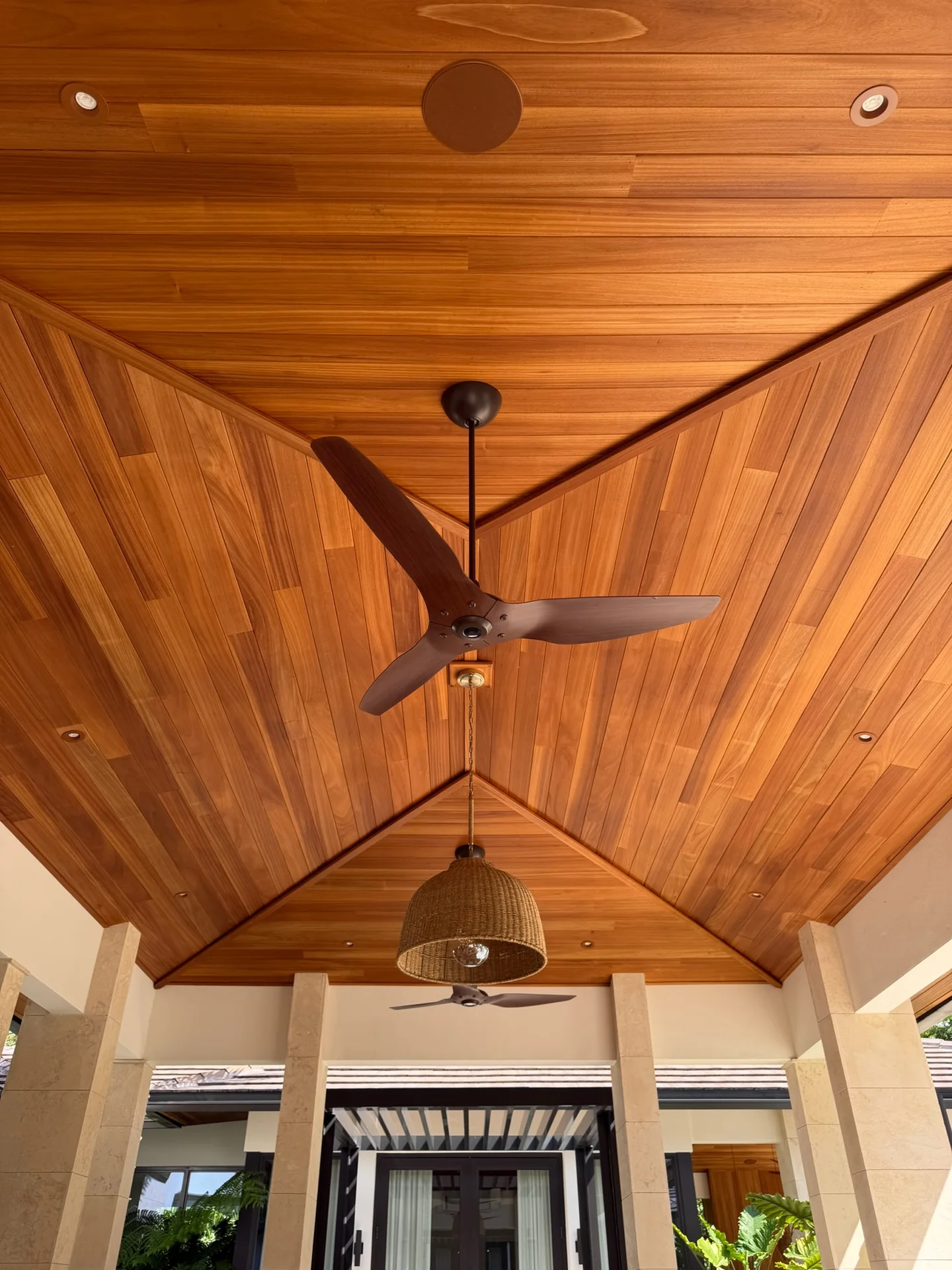 Golden-brown Ayous ceiling above a covered terrace with a dark fan and woven pendant light