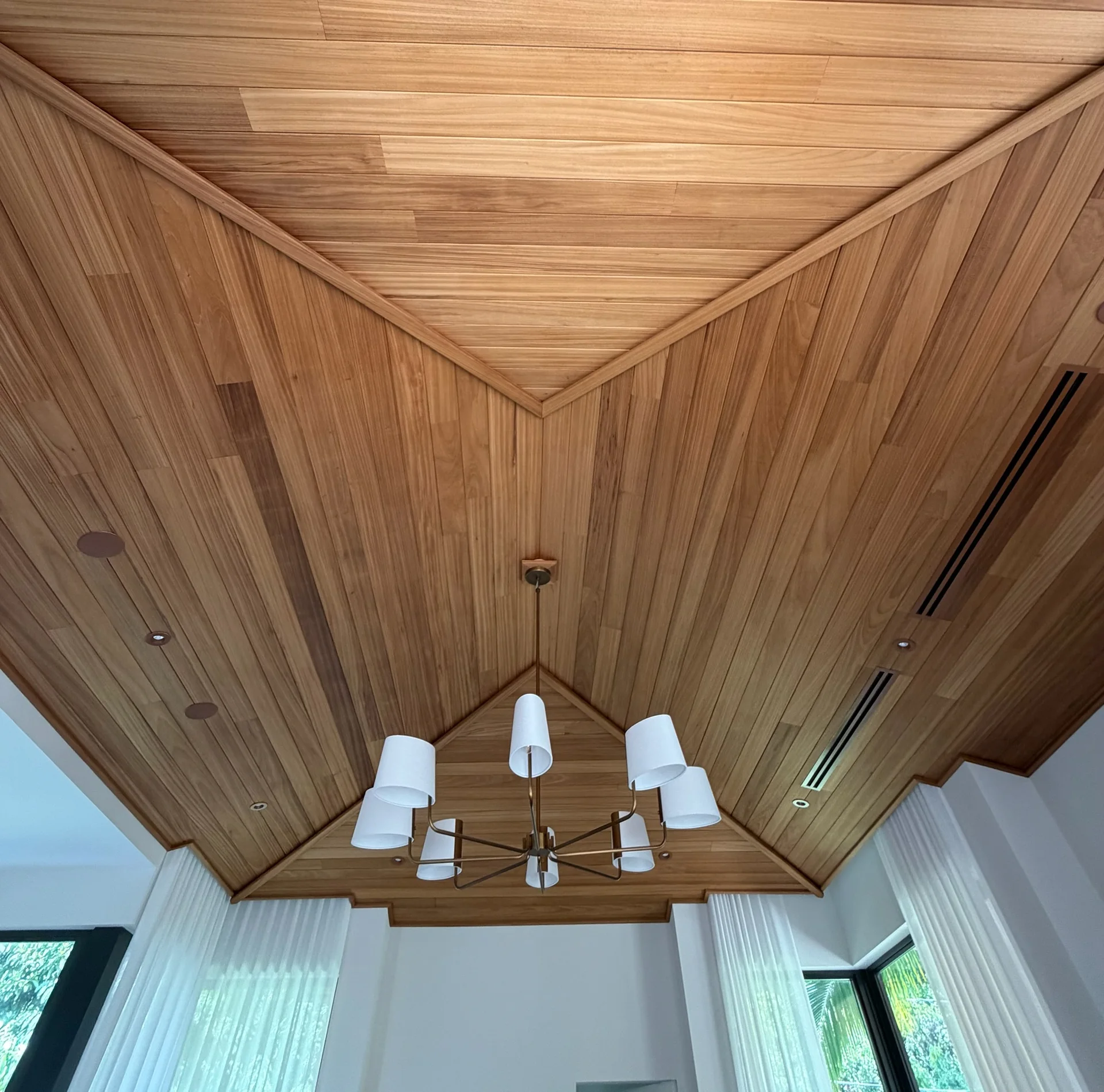 Warm Ayous boards following a faceted ceiling above a shaded chandelier and white curtains