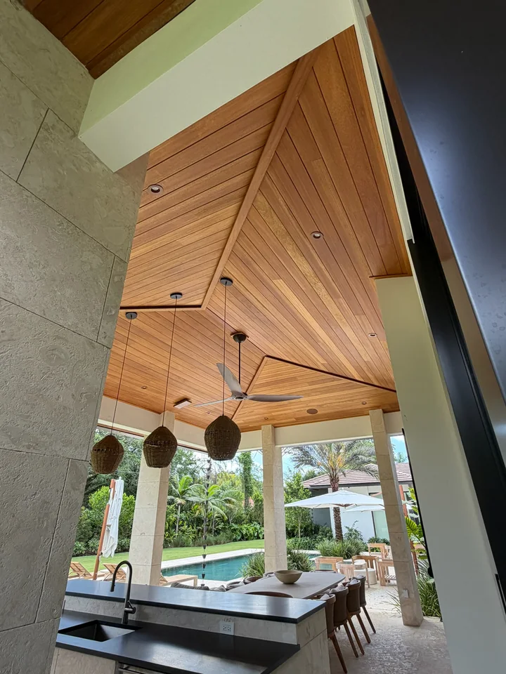 Angled view of an Ayous ceiling over a covered dining area opening toward a pool and garden