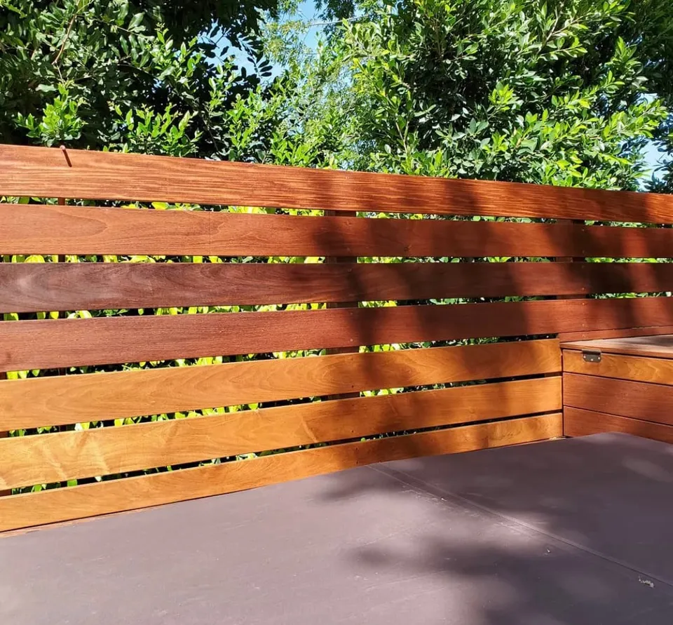 Horizontal wood privacy fence with open gaps and natural grain beside greenery