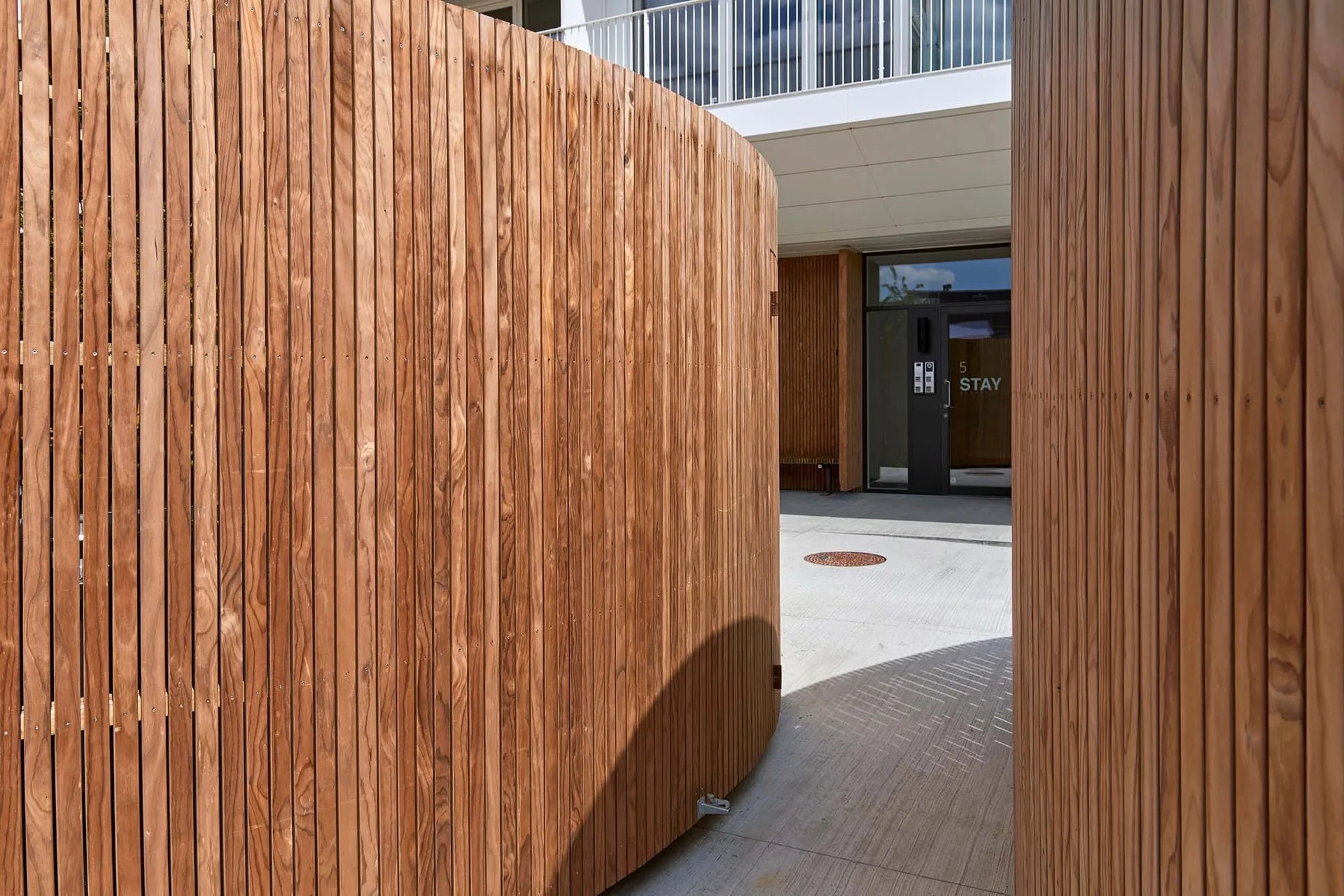 Curved vertical timber-batten screen beside an open paved courtyard