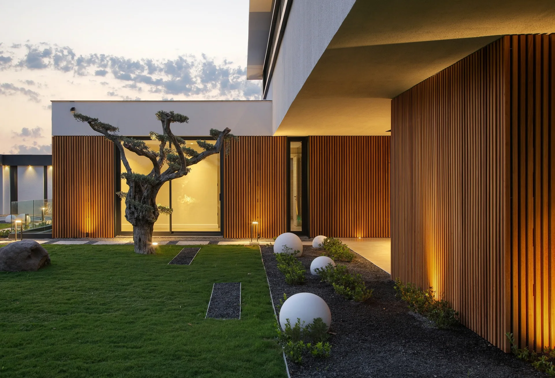 Vertical wood cladding lit from below around a landscaped modern courtyard