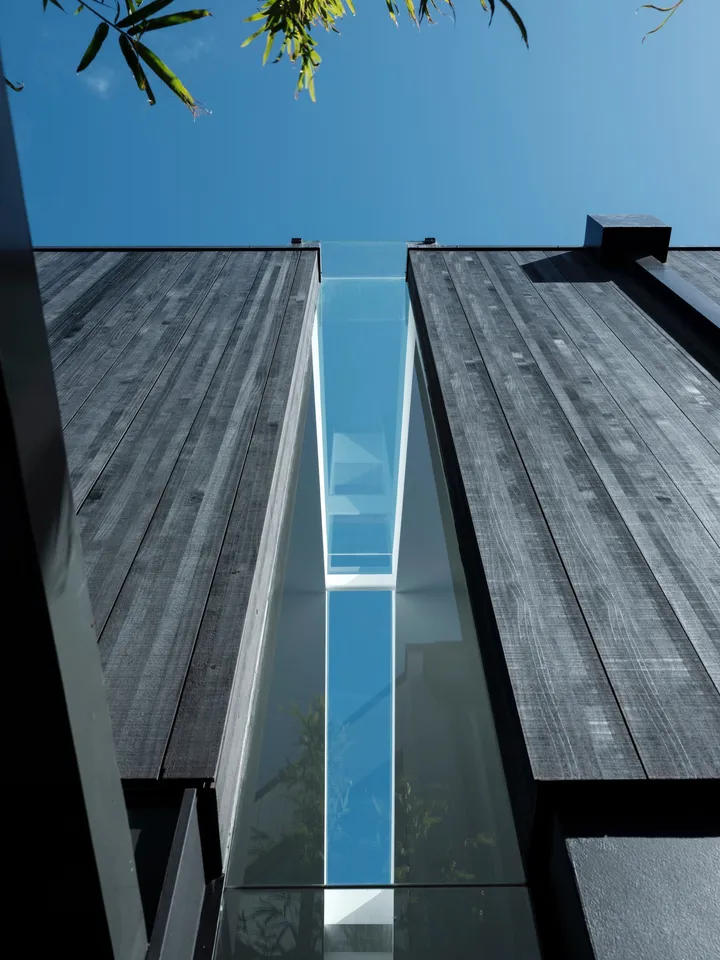 Upward detail of dark vertical wood cladding beside a narrow glazed opening
