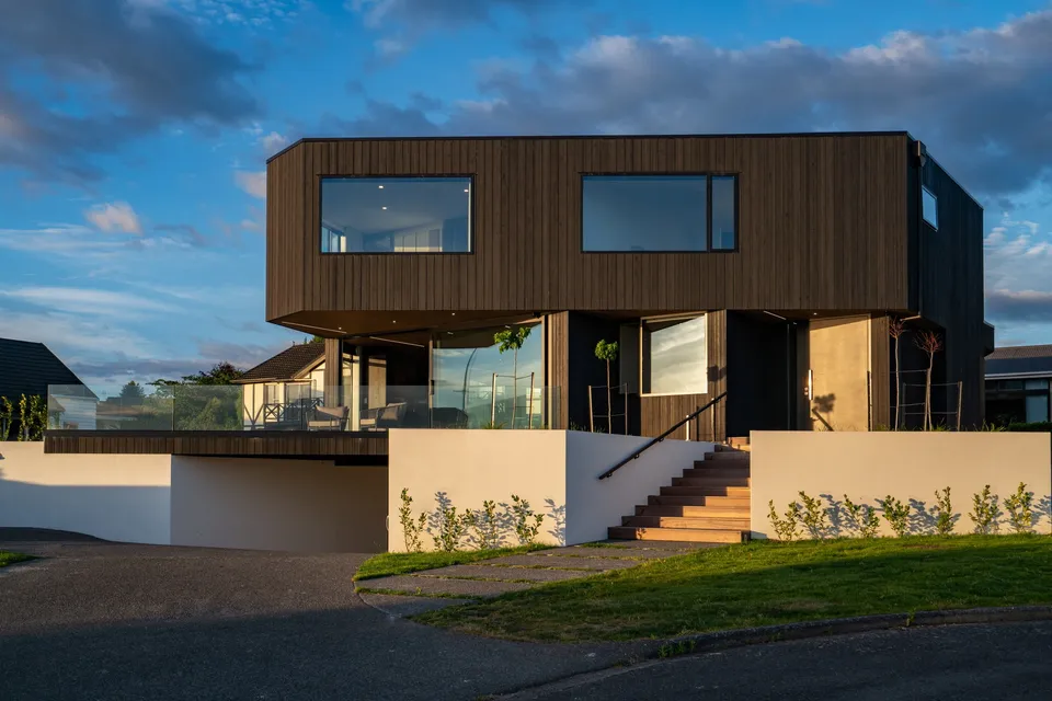 Dark wood-clad upper floor above a glazed living area on a contemporary home