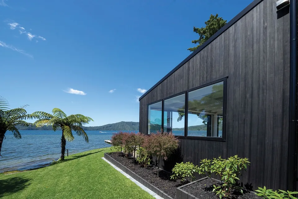 Dark vertical wood siding beside a lake with a long horizontal window