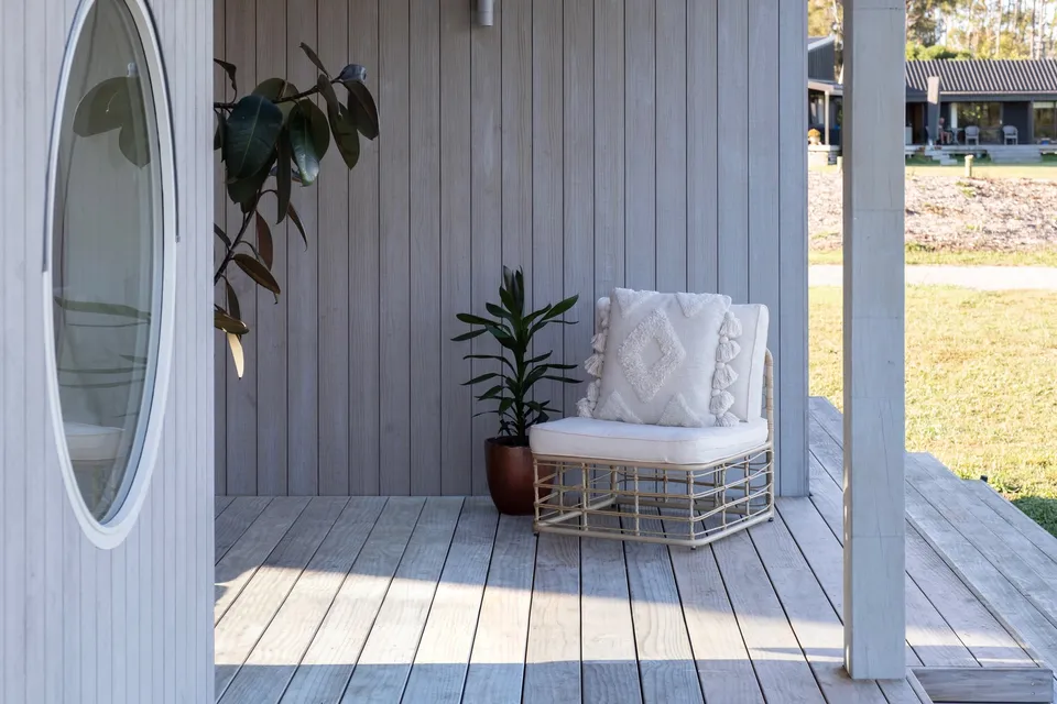 Pale vertical wood cladding surrounding a sheltered porch with a chair and plants