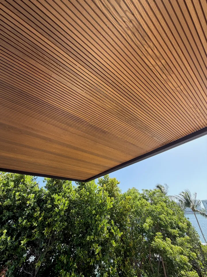 Close view of a finished narrow linear wood soffit with a dark fascia against trees and blue sky