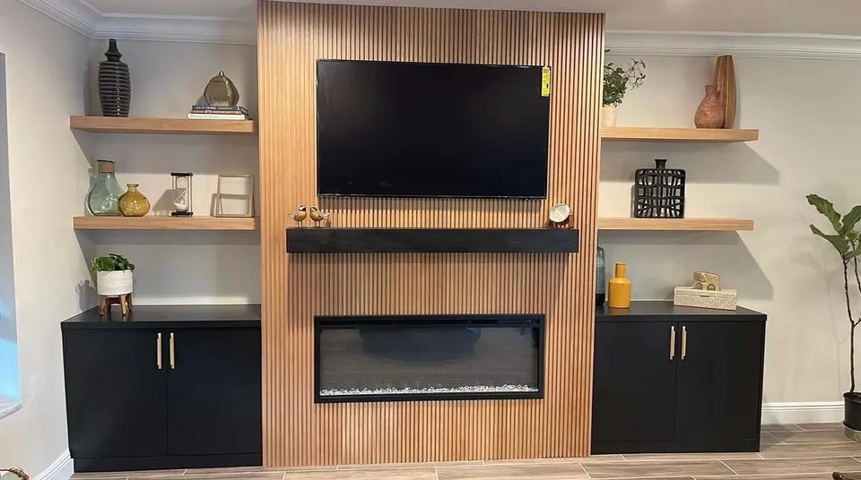 Wood accent wall behind a television and fireplace with shelving on both sides