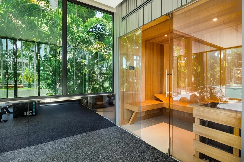 Glass-fronted wood-lined sauna beside a planted, light-filled interior