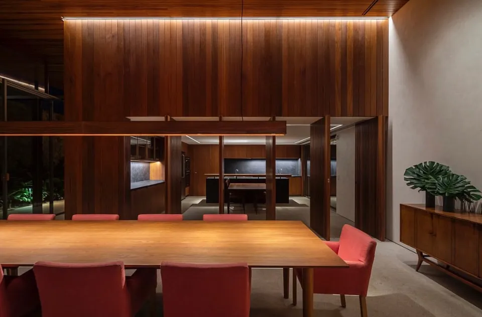 Double-height wood-lined interior with a long table, red chairs and integrated lighting
