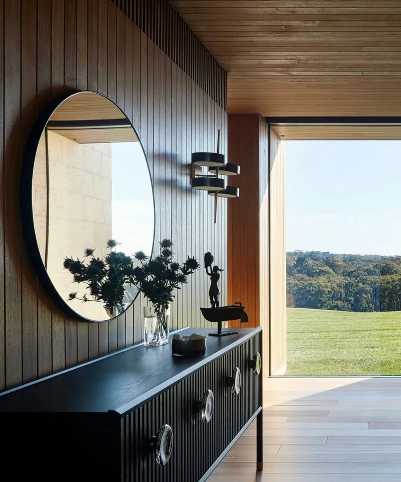 Wood-lined bathroom wall surrounding a circular mirror and dark vanity