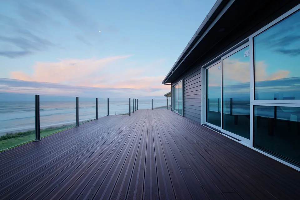 Grooved wood deck beside a glazed coastal home and glass balustrade